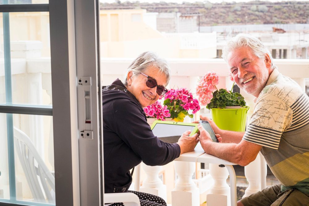 Oudere echtpaar gebruikt een laptop op het terras om hun pensioenportefeuille te beheren met TransFolio.