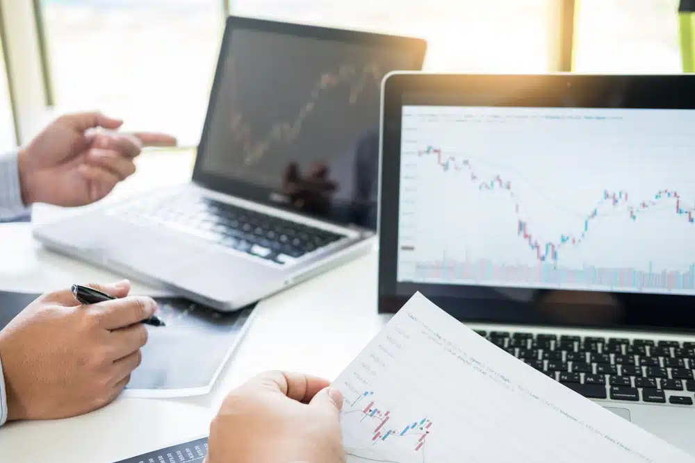Marktanalyse beleggen – twee analisten bespreken koersgrafieken op laptops